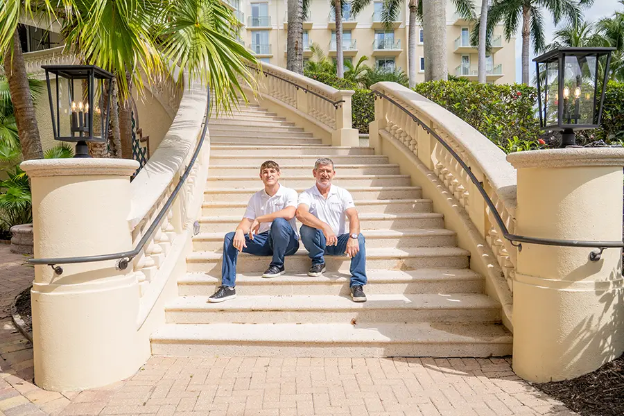 Photo of co-presidents David and Mike Butar sitting on a grand outdoor staircase at a luxury Naples country club.