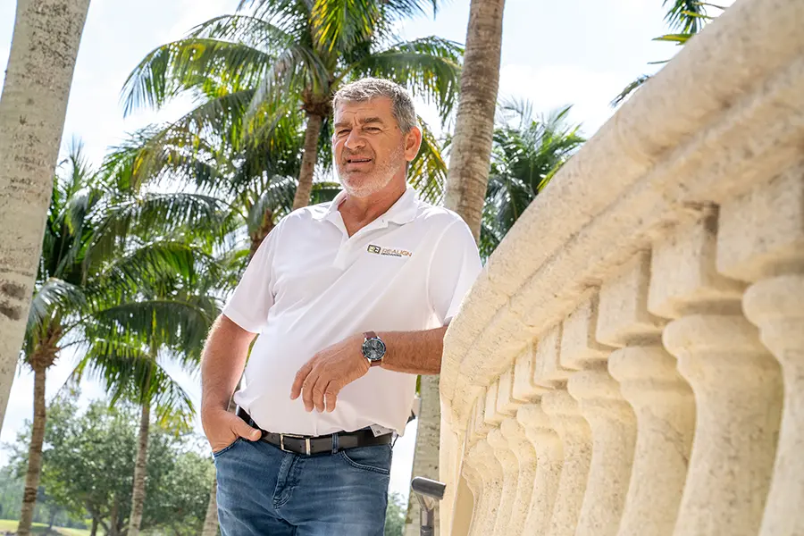 President and design specialist Mike Butar standing outside a country club surrounded by palm trees.