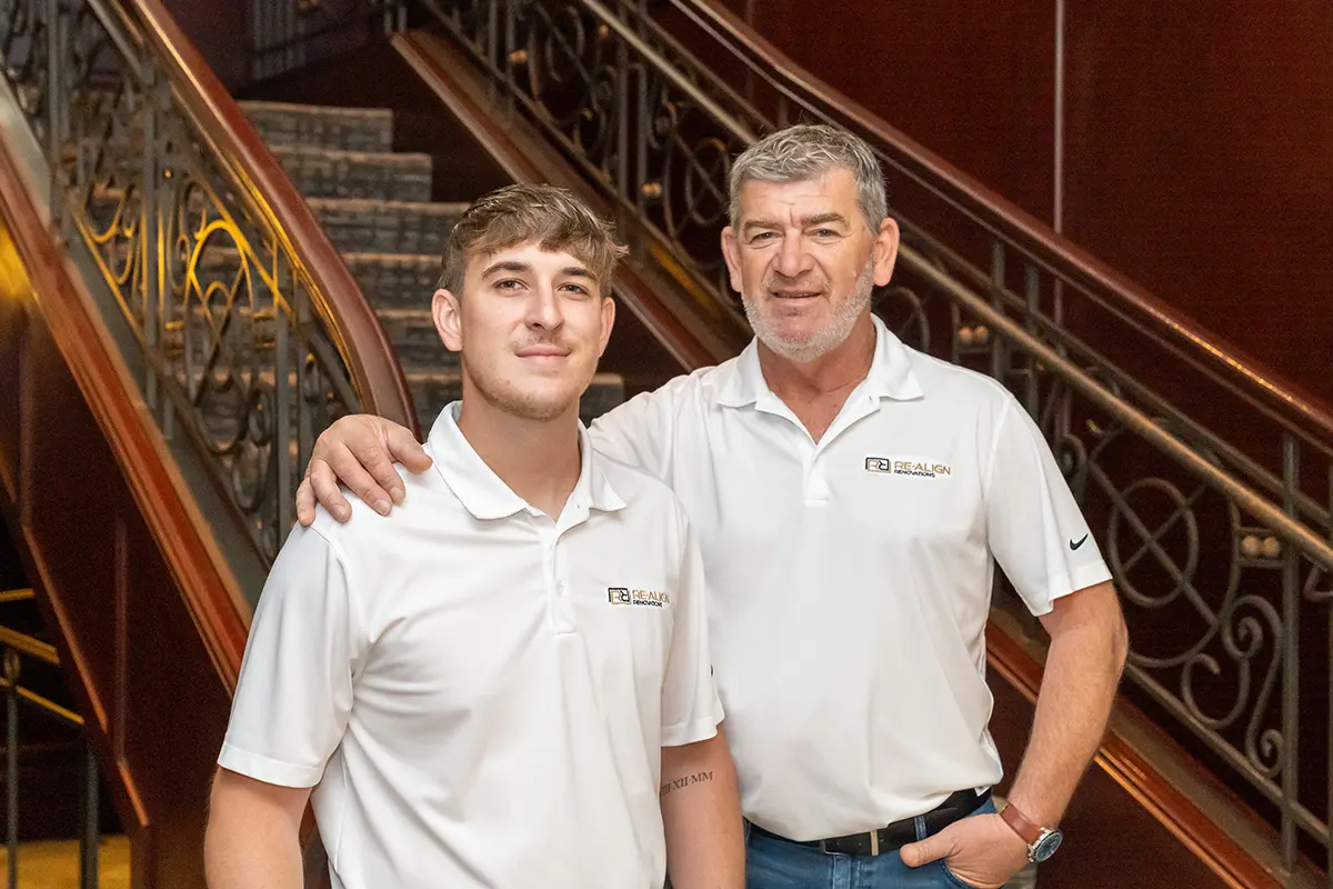 Photo of co-presidents David and Mike Butar wearing their branded polos and standing at the bottom of a grand hotel staircase.